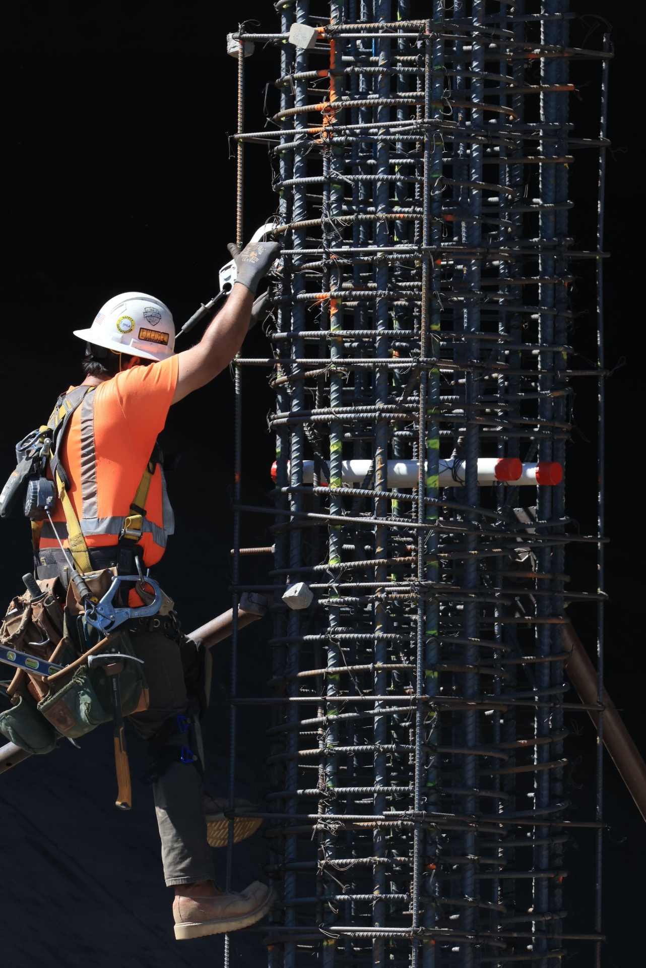 Ironworker in safety harness and hard hat tying rebar on a high-rise jobsite column